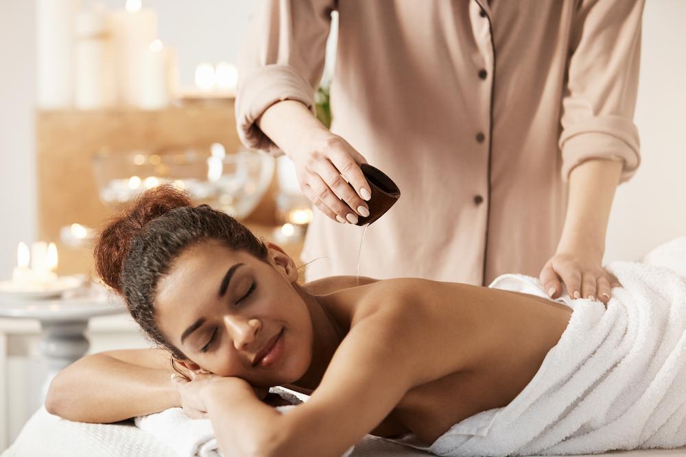 Massagista derramando óleo fazendo massagem para linda mulher africana no salão spa